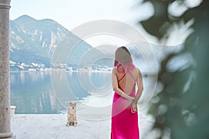 A woman with pink hair in a flowing dress stands with dog