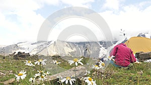 Woman in a pink jacket prepares food near a camping tent, checks if the fire in the burner has gone out among the rocky