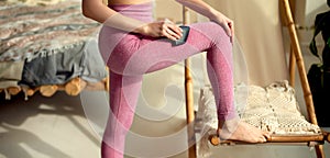 Woman in pink leggings using black comb edge gua sha tool on her leg to relieve muscular tensions. Lower body shot. Physical