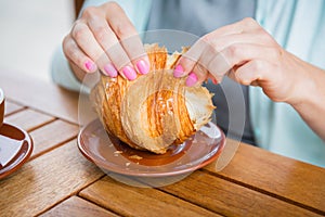 Woman with pink manicure is tearing a small piece from large croissant