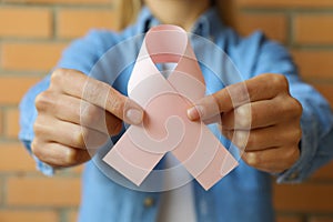 Woman with pink paper awareness ribbon against brick wall background