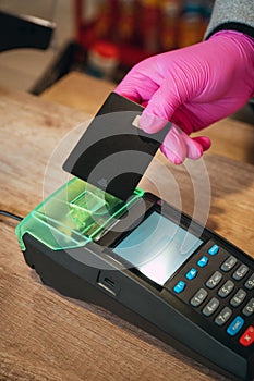 Woman in pink protective glove paying with contactless card at food store during quarantine. Closeup view of terminal