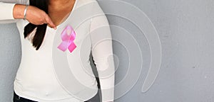 Woman with pink ribbon in her hands and plain gray background for campaign against breast cancer