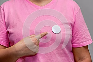 Woman in pink shirt pointing at a shiny round button. Isolated pin badge mockup