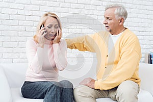 A woman in a pink sweater is sitting on a white sofa and talking worriedly about her smartphone.