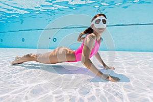 Woman in pink swimsuit with mask posing underwater in pool