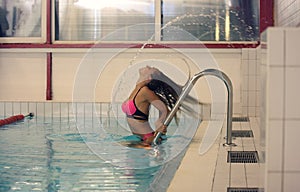Woman in pink swimsuit splashing water with hair in indoors pool