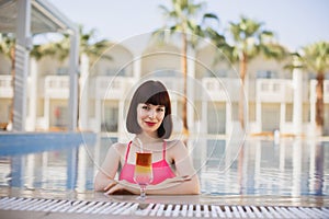 Woman in pink swimwear enjoying swimming in luxury resort pool on sunny summer day with cocktail