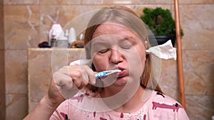 Woman in pink top brushing her teeth with a focus, toiletries and tiles in the background