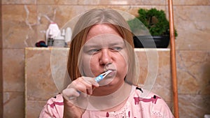 Woman in pink top intently brushing her teeth in a tiled bathroom, seeking solitude