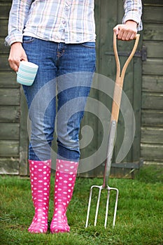 Woman In Pink Wellingtons Holding Garden Fork And Cup