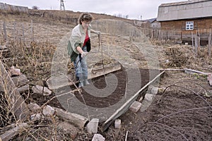 A woman places a greenhouse on a ridge in a vegetable garden, against the backdrop of a village house.