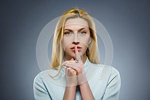 Woman placing finger on lips asking shh, quiet, silence on gray background