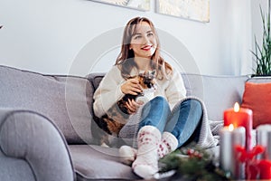 Woman in plaid with tea cup watching movie, TV with cat pet on sofa at home with christmas decoration atmosphere. Lady wear jumper