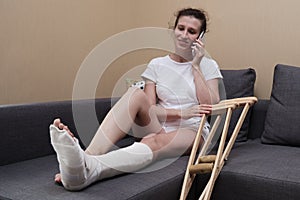 Woman in a plaster cast talking on the phone sitting on a couch in the living room at home