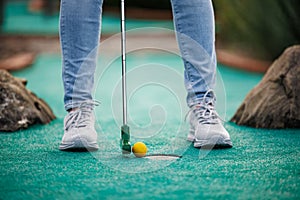 Woman playing adventure or mini golf and trying putting ball into hole