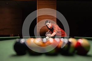 A woman playing billiards at a billiard table, preparing to break a pyramid of multi-colored balls, close-up, selective