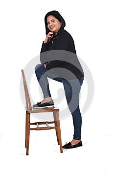 Woman playing with a chair in white background, hand on chin and foot on the chair