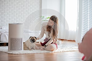 Woman playing with Dog Pug Breed and Air purifier in cozy white bed room for filter and cleaning removing dust PM2.5 HEPA in home