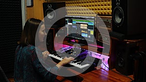 Woman playing on electric piano and creating song at professional recording studio. Female musician plays piano midi keyboard and