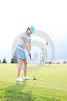 Woman playing golf with female friend holding flag against sky