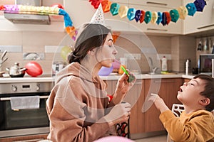 Woman playing with her son with soap bubbles while having fun at the kitchen