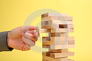 Woman playing Jenga tower on yellow background, closeup