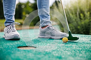 Woman playing mini golf and trying putting ball into hole