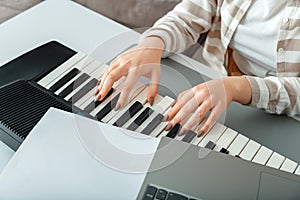 Woman playing piano record music on synthesizer using notes and laptop. Female hands musician pianist improves skills playing