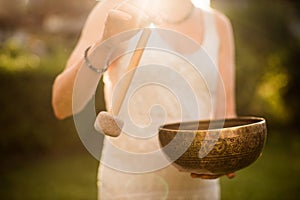 Woman playing Tibetan Singing Bowl with Mallet over Sunset Sky.Relaxing Music Therapy