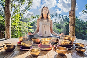 Woman playing on Tibetan singing bowl while sitting on yoga mat against a waterfall. Vintage tonned. Beautiful girl with