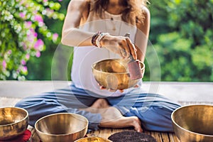 Woman playing on Tibetan singing bowl while sitting on yoga mat against a waterfall. Vintage tonned. Beautiful girl with