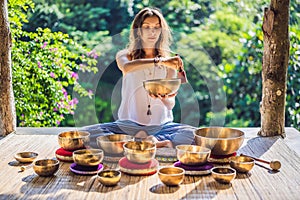 Woman playing on Tibetan singing bowl while sitting on yoga mat against a waterfall. Vintage tonned. Beautiful girl with