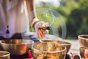 Woman playing on Tibetan singing bowl while sitting on yoga mat against a waterfall. Vintage tonned. Beautiful girl with