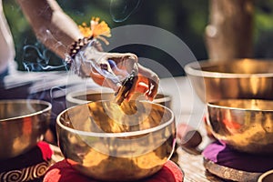 Woman playing on Tibetan singing bowl while sitting on yoga mat against a waterfall. Vintage tonned. Beautiful girl with