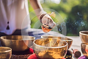 Woman playing on Tibetan singing bowl while sitting on yoga mat against a waterfall. Vintage tonned. Beautiful girl with