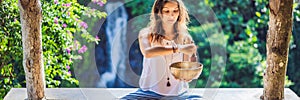 Woman playing on Tibetan singing bowl while sitting on yoga mat against a waterfall. Vintage tonned. Beautiful girl with