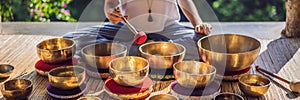 Woman playing on Tibetan singing bowl while sitting on yoga mat against a waterfall. Vintage tonned. Beautiful girl with