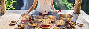 Woman playing on Tibetan singing bowl while sitting on yoga mat against a waterfall. Vintage tonned. Beautiful girl with