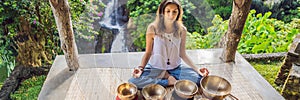 Woman playing on Tibetan singing bowl while sitting on yoga mat against a waterfall. Vintage tonned. Beautiful girl with