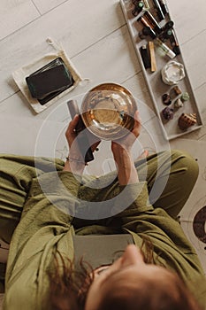 Woman playing on Tibetan singing bowl while sitting on yoga mat. Soft focus blurred and noise effect