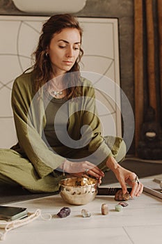 Woman playing on Tibetan singing bowl while sitting on yoga mat. Soft focus blurred and noise effect