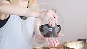 Woman playing on Tibetan singing bowl while sitting on yoga mat. Vintage tonned.