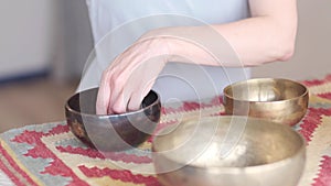 Woman playing on Tibetan singing bowl while sitting on yoga mat. Vintage tonned.