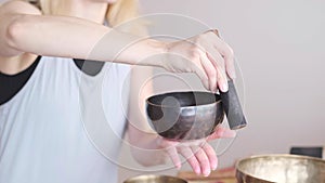 Woman playing on Tibetan singing bowl while sitting on yoga mat. Vintage tonned.