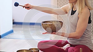 Woman playing on Tibetan singing bowl while sitting on yoga mat. Vintage tonned.