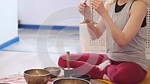 Woman playing on Tibetan singing bowl while sitting on yoga mat. Vintage tonned.