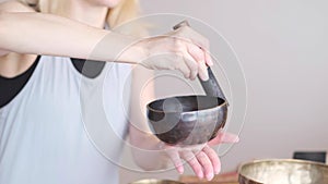 Woman playing on Tibetan singing bowl while sitting on yoga mat. Vintage tonned.