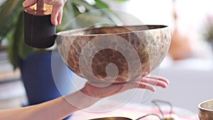 Woman playing on Tibetan singing bowl while sitting on yoga mat. Vintage tonned.