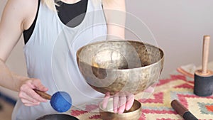 Woman playing on Tibetan singing bowl while sitting on yoga mat. Vintage tonned.